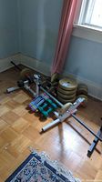 Beige adjustable dumbbells with weight plates stacked, colorful neoprene dumbbells, and exercise frame on wooden floor