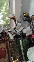 Green golf bag holding various golf clubs with wooden drivers on top and irons inside, with visible wear and scratches.