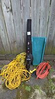Full lot showing Craftsman blower, two extension cords (yellow, orange), and green storage tray against wood fence.