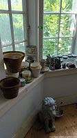 View of window ledge with multiple ceramic pots and planters, animal garden statues, and woven basket planter.