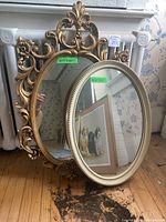 Two oval mirrors placed side by side, one with white beaded frame and one with ornate gold floral frame, sizes labeled.