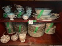 Full shelf showing multiple stacks of teacups on saucers, plates, bowls, and sugar bowl and creamer all with pink floral and gold detailing.