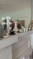 Display of various vases, ceramic tea sets, and decorative items on white mantel including Belleek footed vase with scalloped crown top and other pottery pieces.