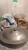 Image of assorted vintage kitchenware and bakeware including an aluminum roasting pan, glass casserole dishes, and measuring spoons.