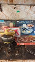 Overview photo showing multiple kitchenware items including yellow cookie press and microwave kitchenware boxes on cooking range.