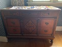 Front view of wooden dresser with carved decorative panels and metal hardware.