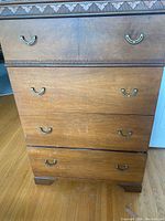 Front view of wooden tallboy dresser showing four drawers with metal handles and visible scratches on wood finish.