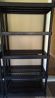Front view of one black plastic shelf unit showing 5-tier slatted shelves and tubular corner supports.