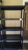 Front view of black plastic garage shelf unit with open slat shelves and tubular support posts.