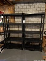 Two black plastic shelving units side by side against a basement wall showing the full height and width.