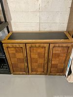 Front view of the checkerboard wood cabinet with black Formica top, showing all three cupboard doors closed.