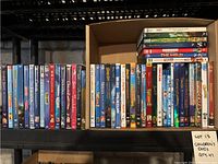 View of multiple children’s DVDs arranged in two rows inside a box, showing titles including Frozen, Toy Story, Finding Nemo, 101 Dalmatians, Barbie movies, Madagascar, and others.