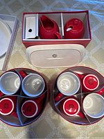 Top view of boxed set showing six red and white mugs, red sugar bowl with lid, and creamer jug in original packaging.