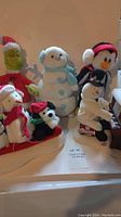 Seven Christmas stuffed animals including the Grinch, snowman with blue earmuffs and scarf, large penguin with red earmuffs, and piano-playing snowman.