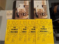 Two hardcover "Our Family History" books and four paperback "The Family Record" books arranged on a table.