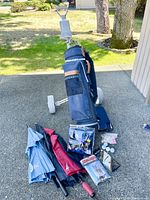 Overall shot showing the blue Spalding golf bag on a roller cart with multiple umbrellas and golf accessories laid out in front.
