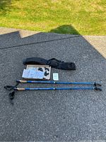 Pair of blue KEEN FIT walking poles with cork handles and carrying case laid out on pavement with instruction papers and pole tips.
