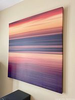 Side angle view of a large square canvas wall art showing abstract sunset colors in orange, yellow, brown, and purple hues.