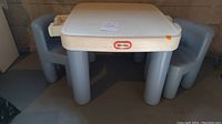 Little Tikes plastic activity table with two drawers and two gray plastic chairs, all placed on concrete floor.