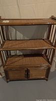 Front view of the bamboo and rattan shelf unit showing two doors, three shelves, and overall design.