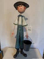 Full view of the metal farmer figurine holding a black metal bucket, showing the overall height and attire.