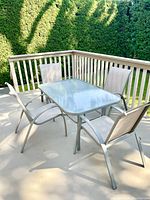 Full view of rectangular glass patio table with four matching arm chairs on a patio.