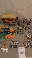 Overview of the entire Playmobil African Safari set showing the safari lodge, jeep vehicle, animal figures including elephants, hippopotamus, zebra, giraffe, polar bear, lion, leopard, rhino, and multiple human figures and a small pond accessory.