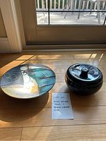 Raku bowl and black lidded dish on hardwood floor, note indicating lot contents