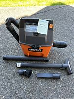 Front view of RIDGID shop vac with hose connected and accessories displayed in front on pavement.