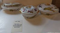 Three porcelain Royal Worcester covered casserole dishes with Evesham Gold fruit and vegetable pattern and gold trimming, displayed on a table with label card.
