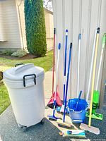 Rubbermaid garbage can and assortment of cleaning tools arranged outside.