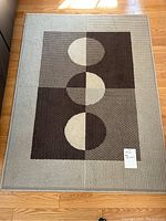 Full view of rectangular rug showing geometric pattern of circles and blocks in brown, beige, and gray on wood floor