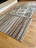 Two abstract wave plush rugs beside geometric thin pile rug on hardwood floor.