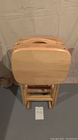 Four pine wood folding TV trays stacked in folded position with a stand behind them, showing size and shape.