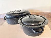 Two black speckled roasting pans with lids, oval pan larger in back, round pan smaller in front