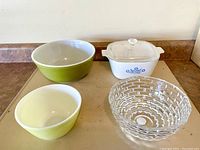Four vintage kitchen items on countertop: green Pyrex bowl (#403), citron yellow Pyrex bowl (#401), white and blue Corningware 1.75 qt casserole dish with lid, textured clear crystal bowl