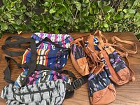 Five vintage Azteca tapestry bags arranged on a wooden table next to green shrubbery, showing two fanny packs and three small handbags with leather details.