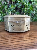 Front angle view of the octagonal brass cricket box with reticulated ventilation pattern, clasp, and handle on the lid.