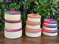 Photo of nine vintage handwoven natural fiber baskets arranged in three groups of three, showing their varying sizes and colorful trims.