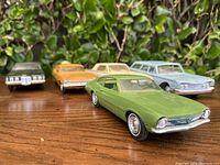 Five vintage Hubley Ford diecast model cars displayed on wood surface with green shrubbery background; front view showing detailed front ends of the cars
