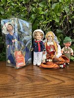 Four vintage international dolls including a boxed doll in blue, a sailor boy doll, a seated female doll in traditional dress, and a small boy doll in lederhosen.