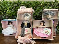 Four vintage Madam Alexander dolls in original boxes with protective plastic wraps. Dolls displayed outdoors with green shrubbery background. Dolls include Scarlett, Beth, Rhett, and Lord Fauntleroy characters.