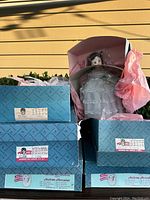 Three vintage Madame Alexander dolls in original blue patterned boxes with pink tissue paper, displayed outside against wooden wall.