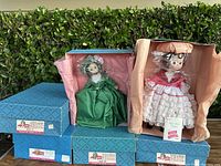 Four vintage Madam Alexander dolls in original blue and beige boxes, two dolls visible dressed in period costumes with packaging and tags.