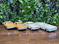 Front and side view of four vintage promo model cars, two mustard yellow and two off-white.
