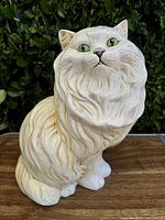 Front view of cream-colored ceramic Persian cat figurine showing detailed fur and green eyes.