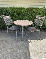 Full set outdoor bistro patio set featuring round mosaic stone table with two metal chairs.