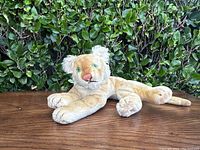 Front perspective of the vintage Steiff lion cub stuffed toy on wooden surface with foliage background.