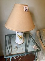 Photo of a single vintage ceramic base lamp with beige conical shade, showing painted yellow flowers and green leaves on white ceramic.