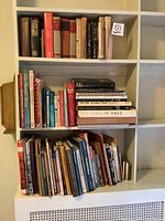 Three shelves filled with assorted books of varying sizes and colors, predominantly hardcover with some paperbacks visible. Books include literature, reference, and general interest titles.
